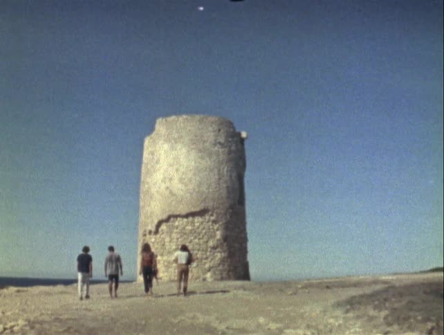 Group of people walk towards an ancient cylindrical stone tower under a clear sky