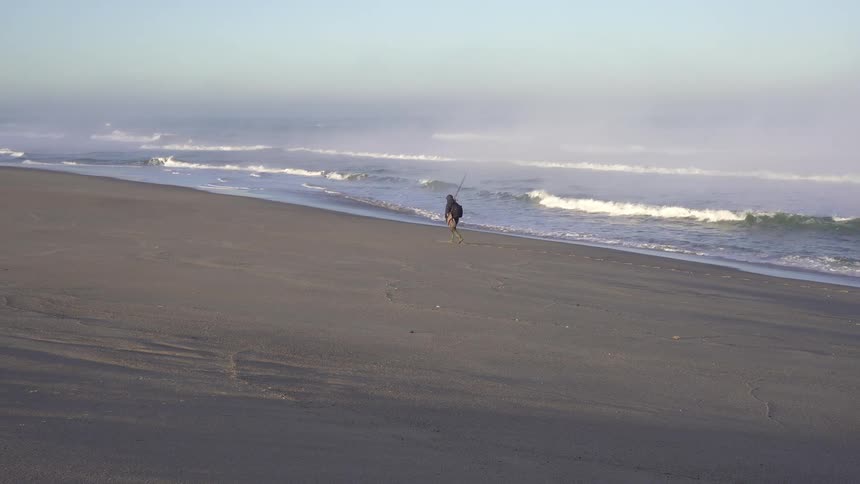 Fisherman walks on the sand of the beach with the sea next to him