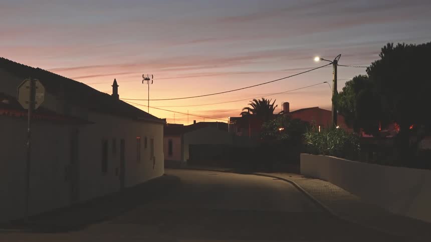 A street scene at dusk with houses on either side and a sky with hues of pink and blue
