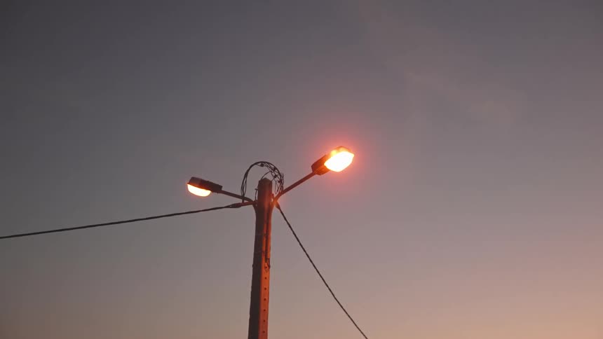 A streetlamp glowing at dusk with power lines stretching out from it