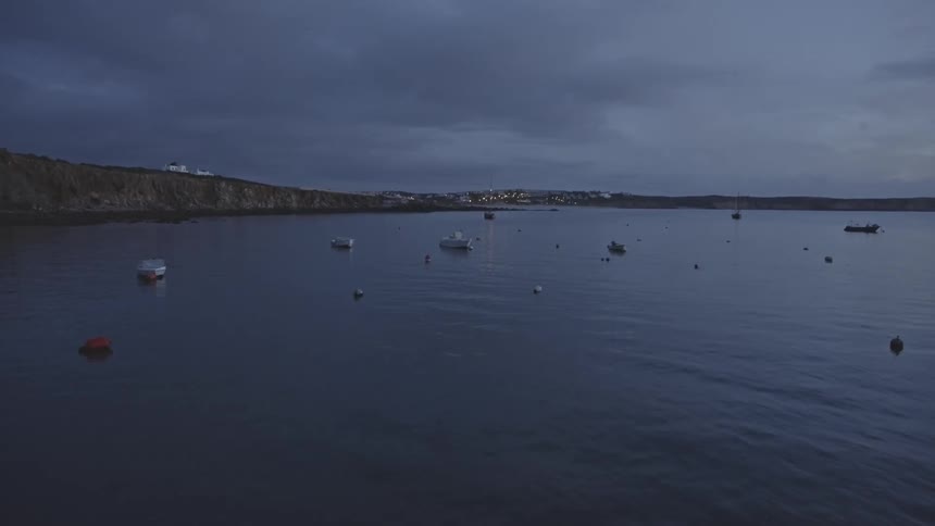 Various boats float in the waters off of a coastline and village