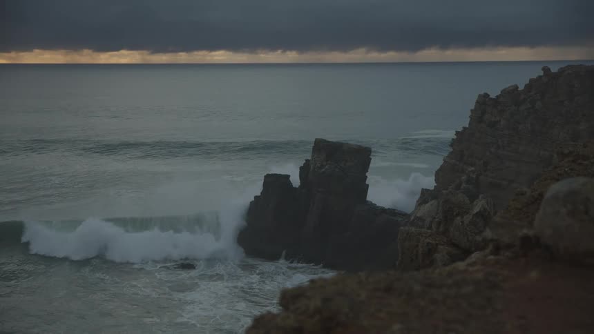 Ocean waves crash against a rocky coastline at sunset