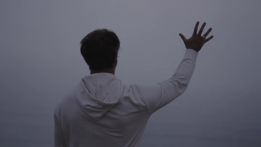 Person from behind wearing a white hoodie reaching out with one hand towards a foggy background