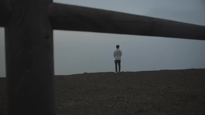 View through a wooden fence with a man standing on a rocky shore