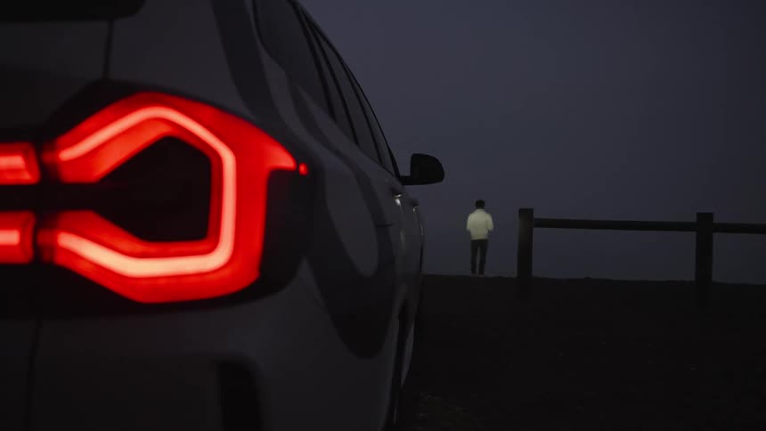 Headlights on the back of a vehicle and in the background a person standing in a place at night