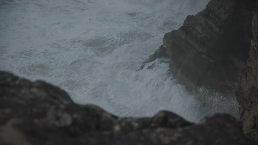 Strong waves with foam crashing against the rocky coast