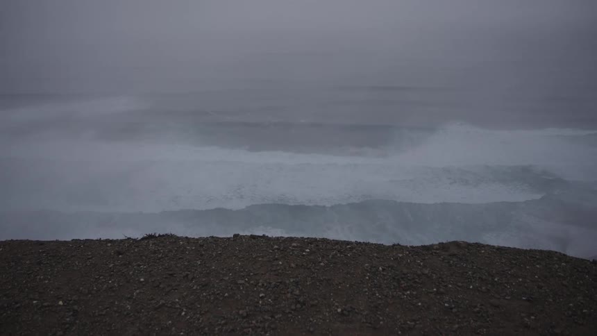 A vast body of water under a foggy or misty atmosphere with a strip of land in the foreground