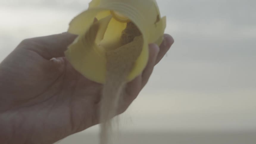 Hand picking up plastic trash from the sand