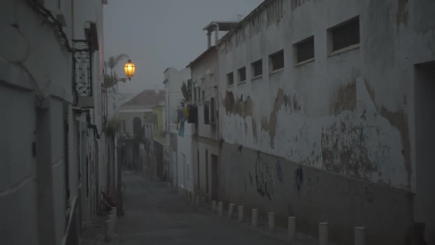 A narrow street between aged buildings with peeling paint under a dusky or overcast sky