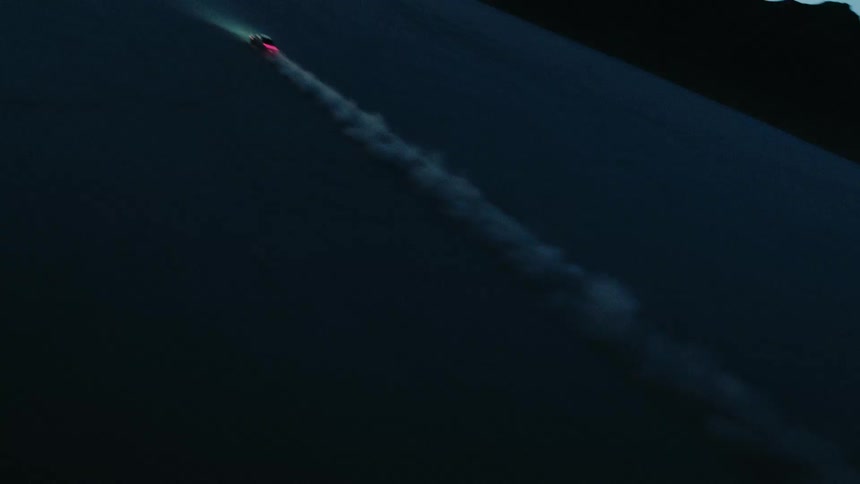 Vehicle at a distance leaving a trail of dust as it travels across a vast flat expanse