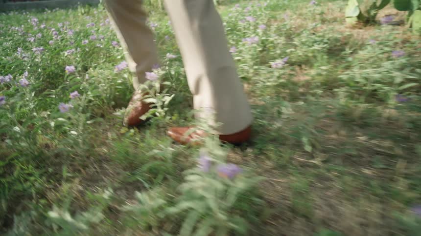 A man wearing slacks and boots walks and spins around in a field filled with flowers