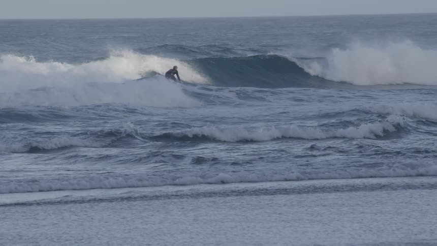 A person surfing on a wave in the ocean visible against the spray of water at the crest of the wave