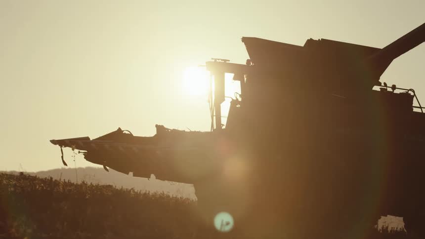 A person drives a harvester across a fallow farm field
