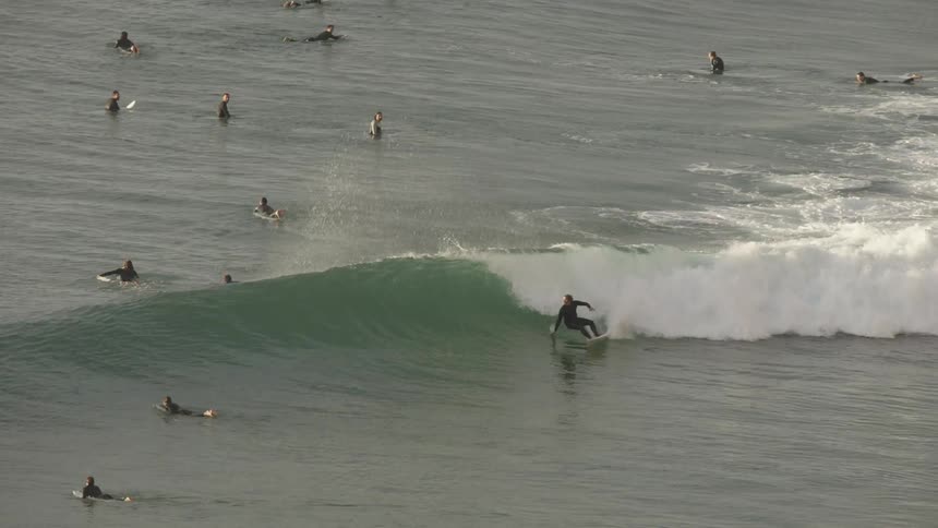 Surfers in the sea with one of them surfing a wave and doing maneuvers