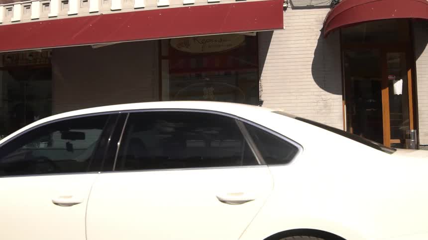 A teenager skateboards down a sidewalk near parked cars and pedestrians walking by businesses