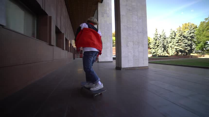Young person skateboarding in an outdoor hallway during daytime