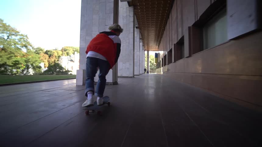 Young person skateboarding in an outdoor hallway during daytime