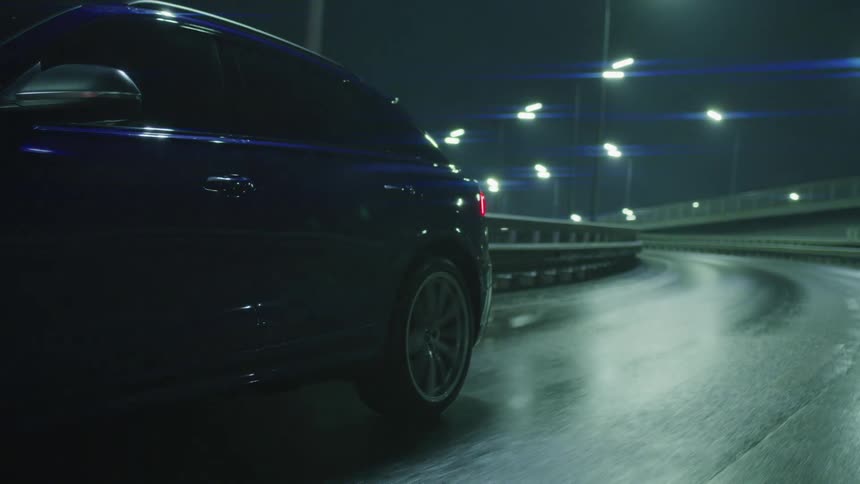 A blue sedan drives down a wet highway at night