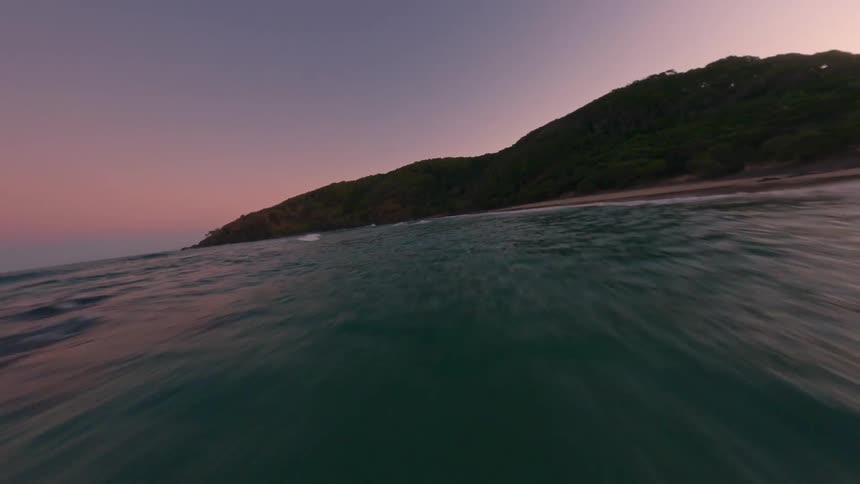 An aerial view of a coastline during twilight with waves crashing onto the shore