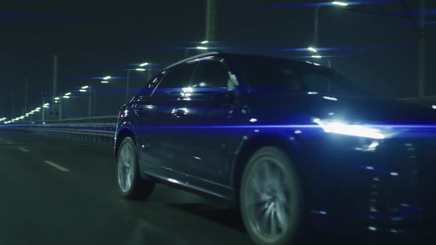 A blue car driving on a highway at night illuminated by streetlights