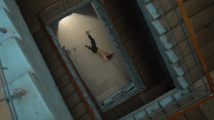 A shirtless male dancer performs some moves at the bottom of a building stairwell