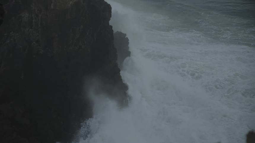 A dramatic wave crashes against a dark cliff