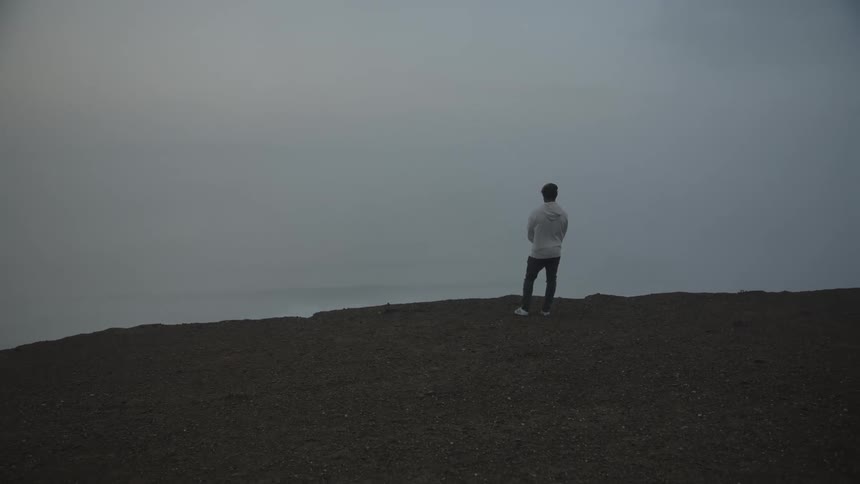 Person standing on a cliff enjoying the seaside view on a cloudy day