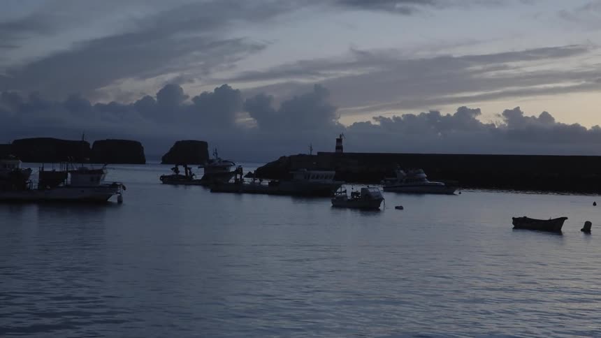 Seascape with silhouette of boats against a cloudy purple sky at dawn