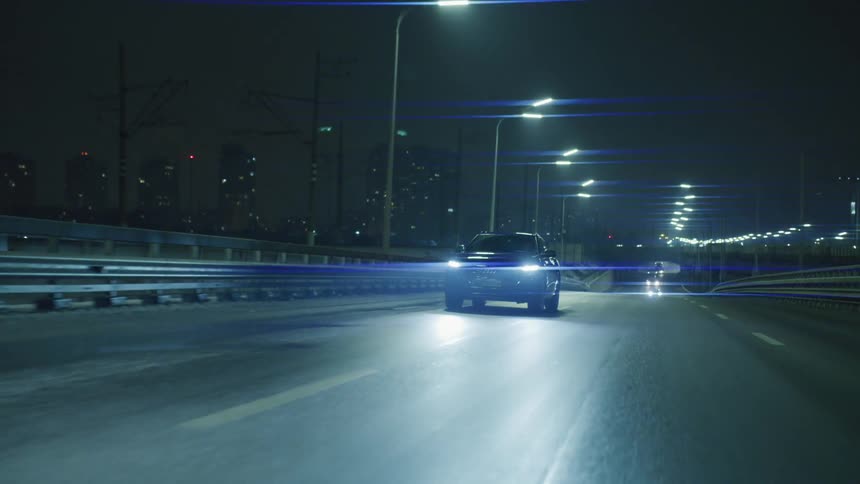 A car drives down a city street lit by streetlights at night