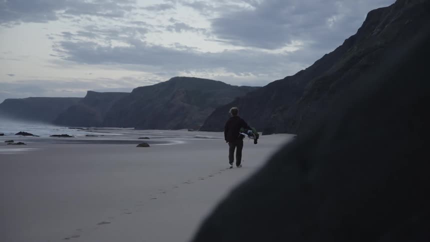 Woman leaves footprints in the sand at the beach near the mountains