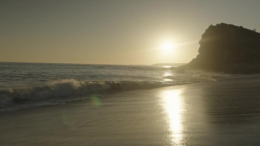 A sunset at a beach with the sun near the horizon casting a warm glow over the water and wet sand