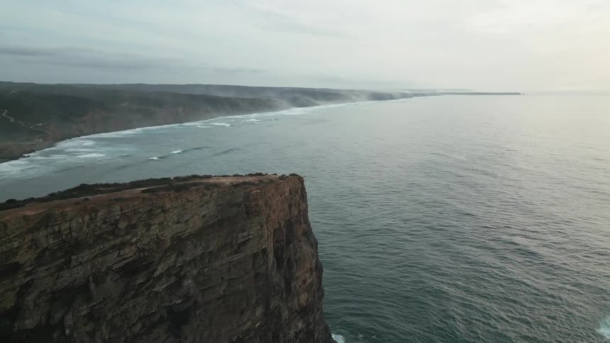 Aerial of ocean waves crashing into steep cliffs