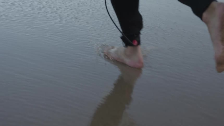 Feet of a surfer running on the wet sand towards the sea