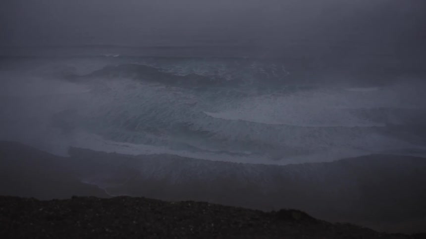 A dark and moody seascape with waves rolling in under an overcast sky captured from a high vantage point