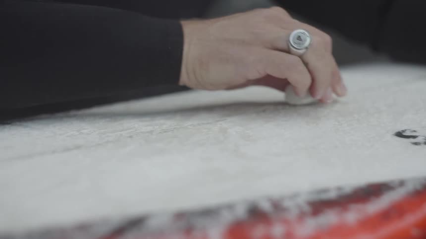 Closeup of an adult waxing a surfboard
