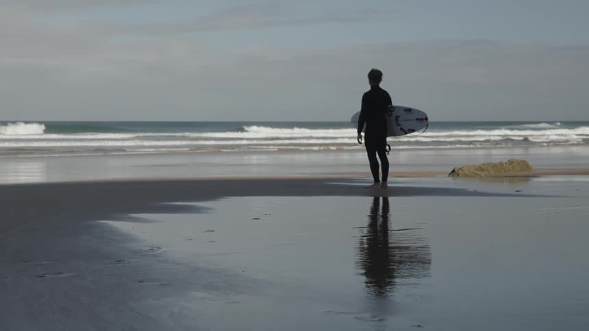 Surfer with his surfboard standing in front of the sea on the beach