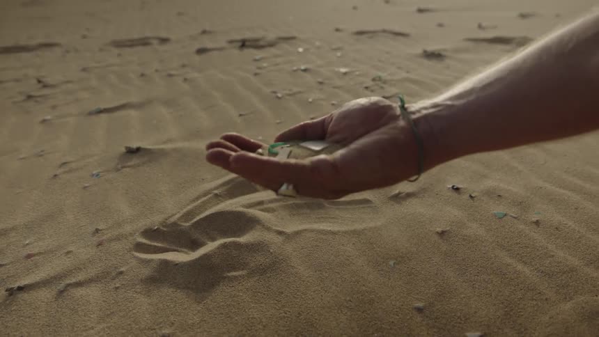 A man shakes glass from a handful of sand