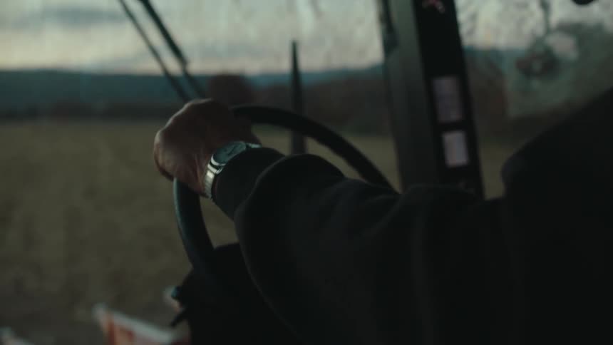 Closeup of an adult driving a tractor through a field