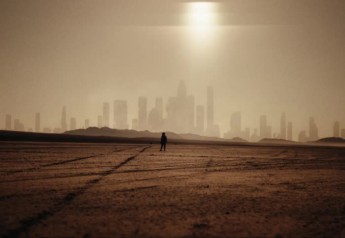 Silhouette of a person walking through the desert with the sun and skyscrapers in the background