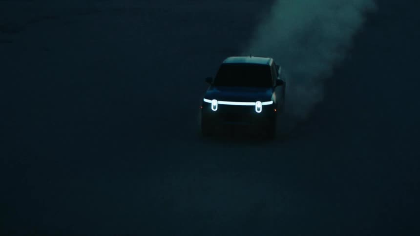 A car kicks up dust driving across a plain far away from a downtown city area