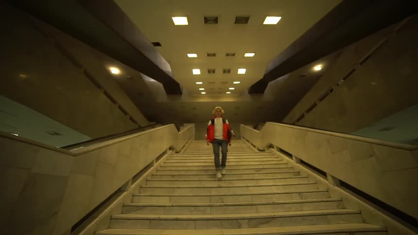 Blonde skateboarder climbs down a wide staircase carrying a skateboard