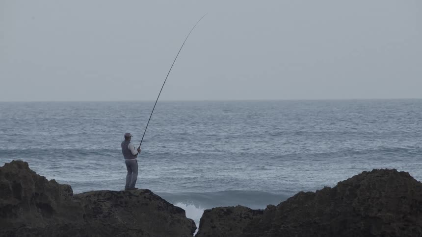 Man on top of a rock fishing in a vast ocean