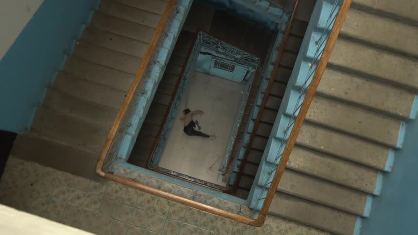 Topdown view of a staircase with a person breakdancing on the landing below