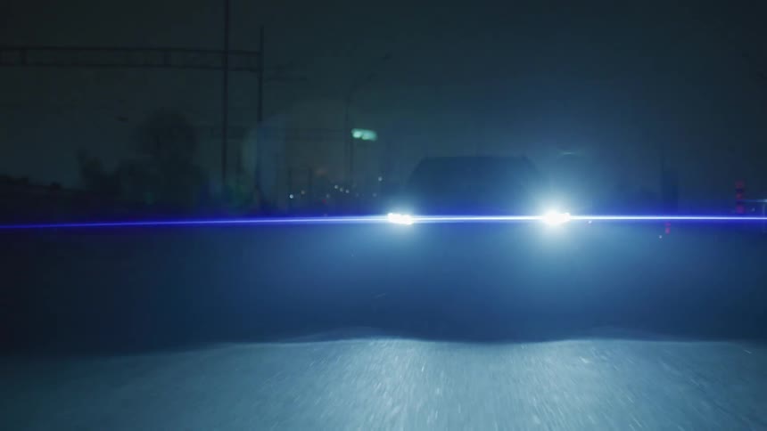 View of a car traveling down a street at night with its headlights on