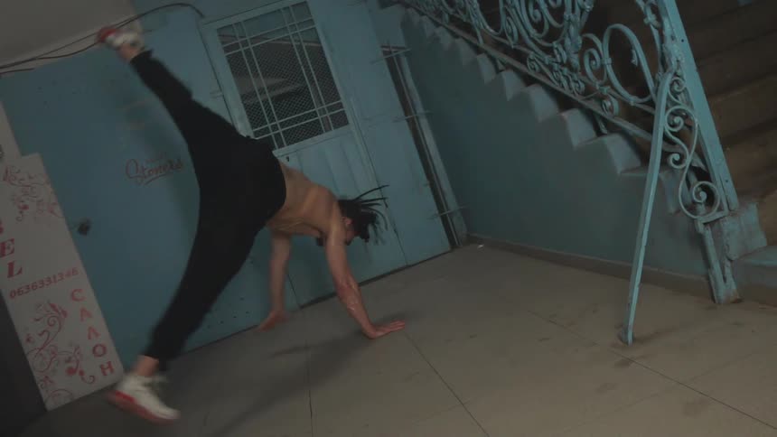 A fit shirtless young man breakdancing in a corridor