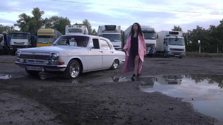 A woman walks through a lot past a jumping car