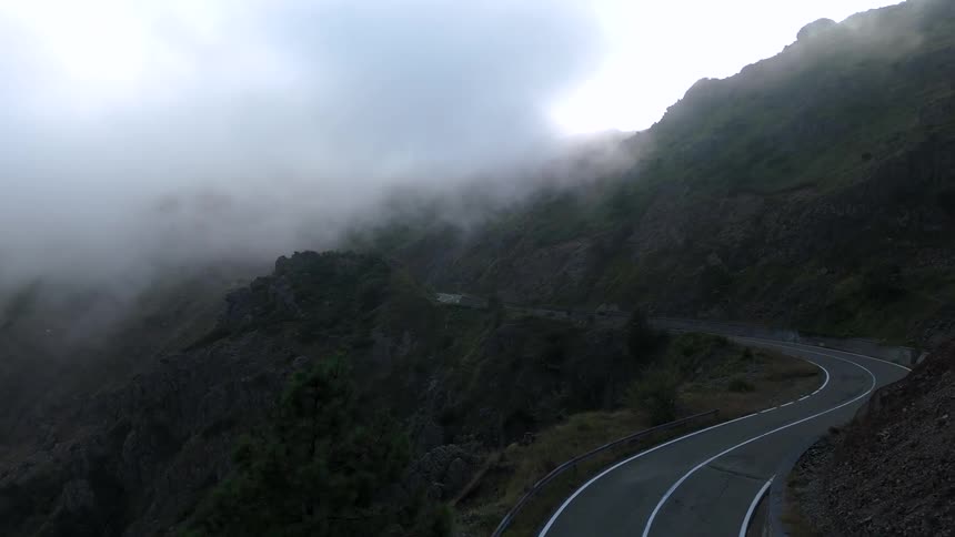An aerial view of a winding road snaking through a foggy mountain pass