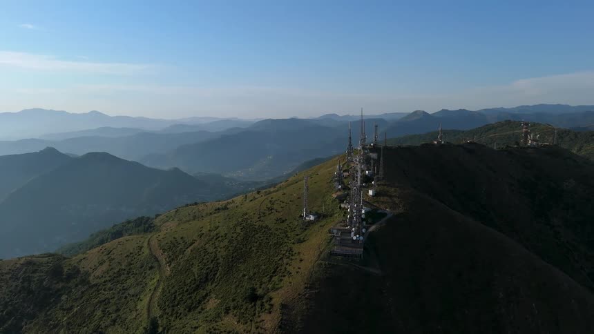 A series of white communication towers atop a green rolling hill with a clear blue sky in the background