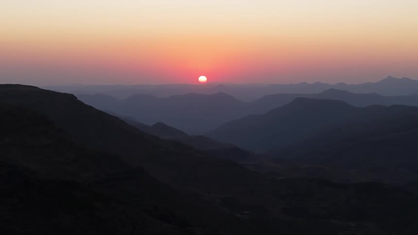 The sun shines over multiple mountain ranges