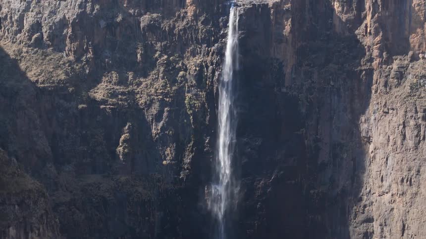 A towering waterfall cascading down a steep rocky cliff with barren cliffs
